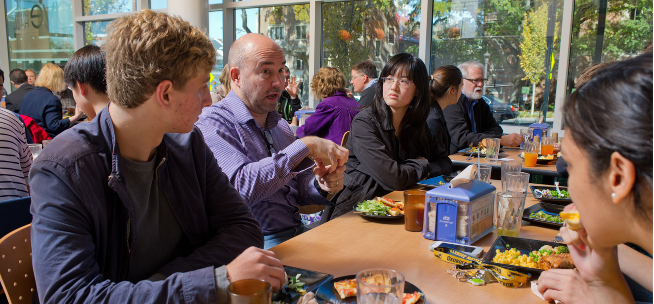 people speaking to each other sitting at a table eating