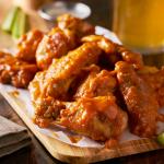 sauced buffalo chicken wings on wooden board with celery