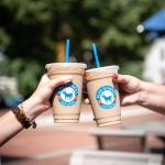 two hands holding iced coffee cups together with outside background